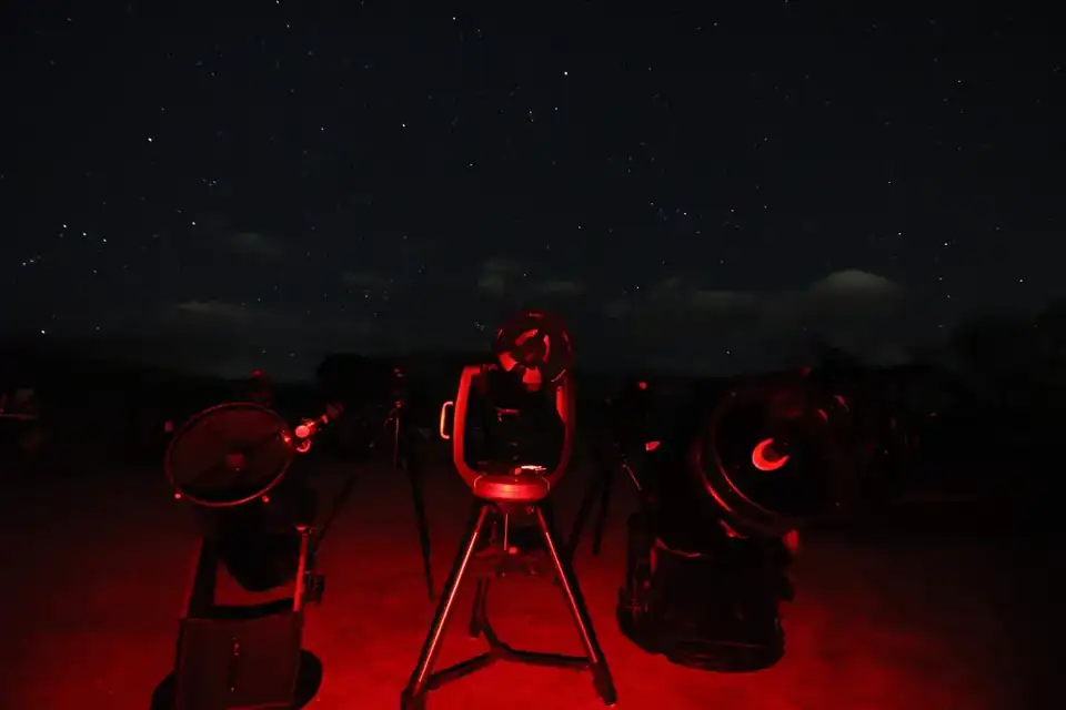 Several telescopes set up beneath the stars with dim red observing lights during an AstroTours.org program.